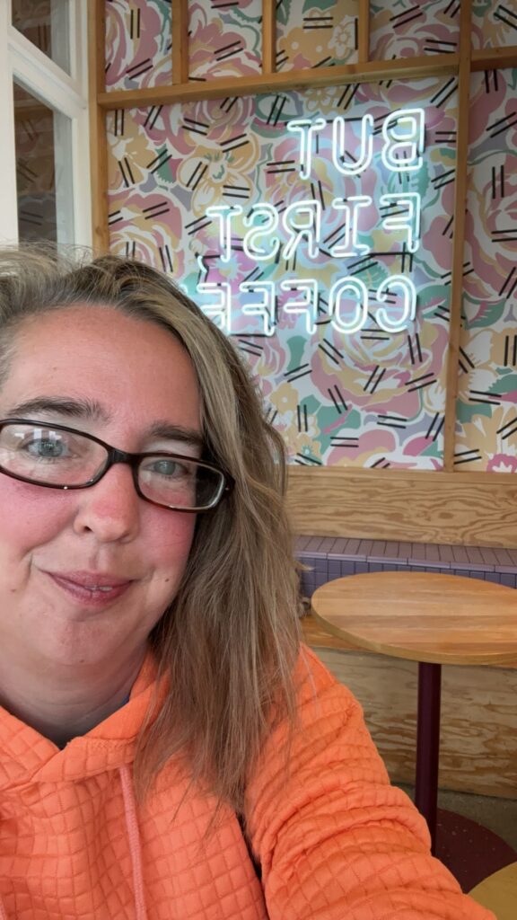 A person (me) in front of a "but first coffee" sign at Alfred's Coffee Shop in Venice Beach