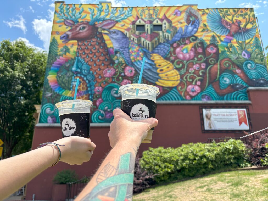 Two cold coffees being held up infront of a mural