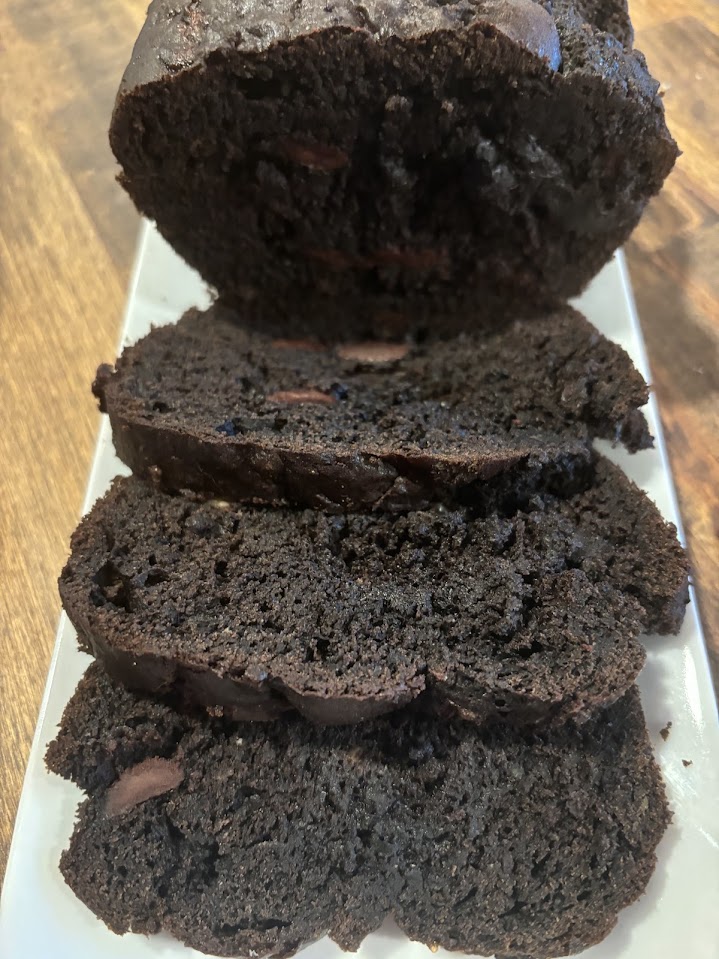 Three slices and then the rest of a chocolate zucchini bread on a white plate with a wood table underneath