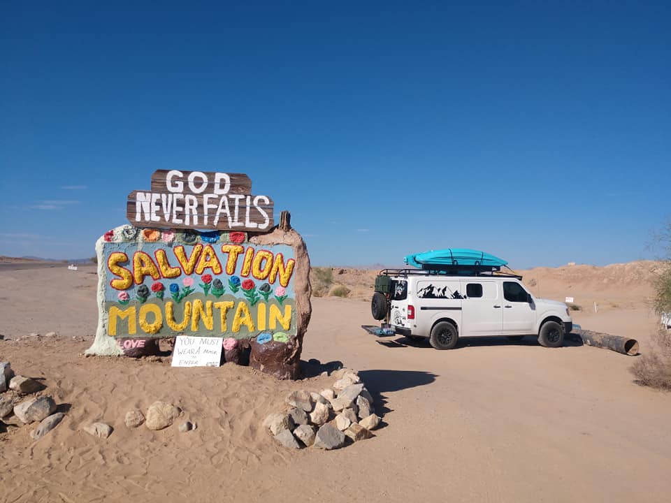 A big boulder with Salvation Mountain written on it with a Nissian NV1500 in the background