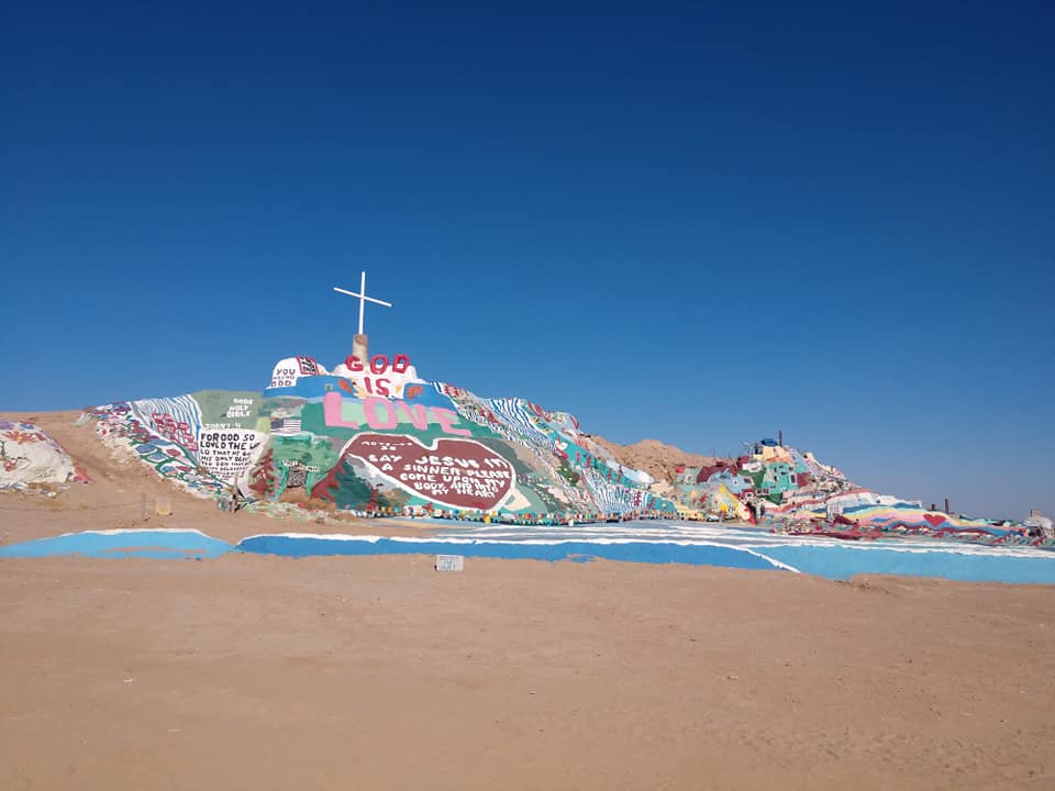 A cross sitting on top of a painted mountain in the California dessert