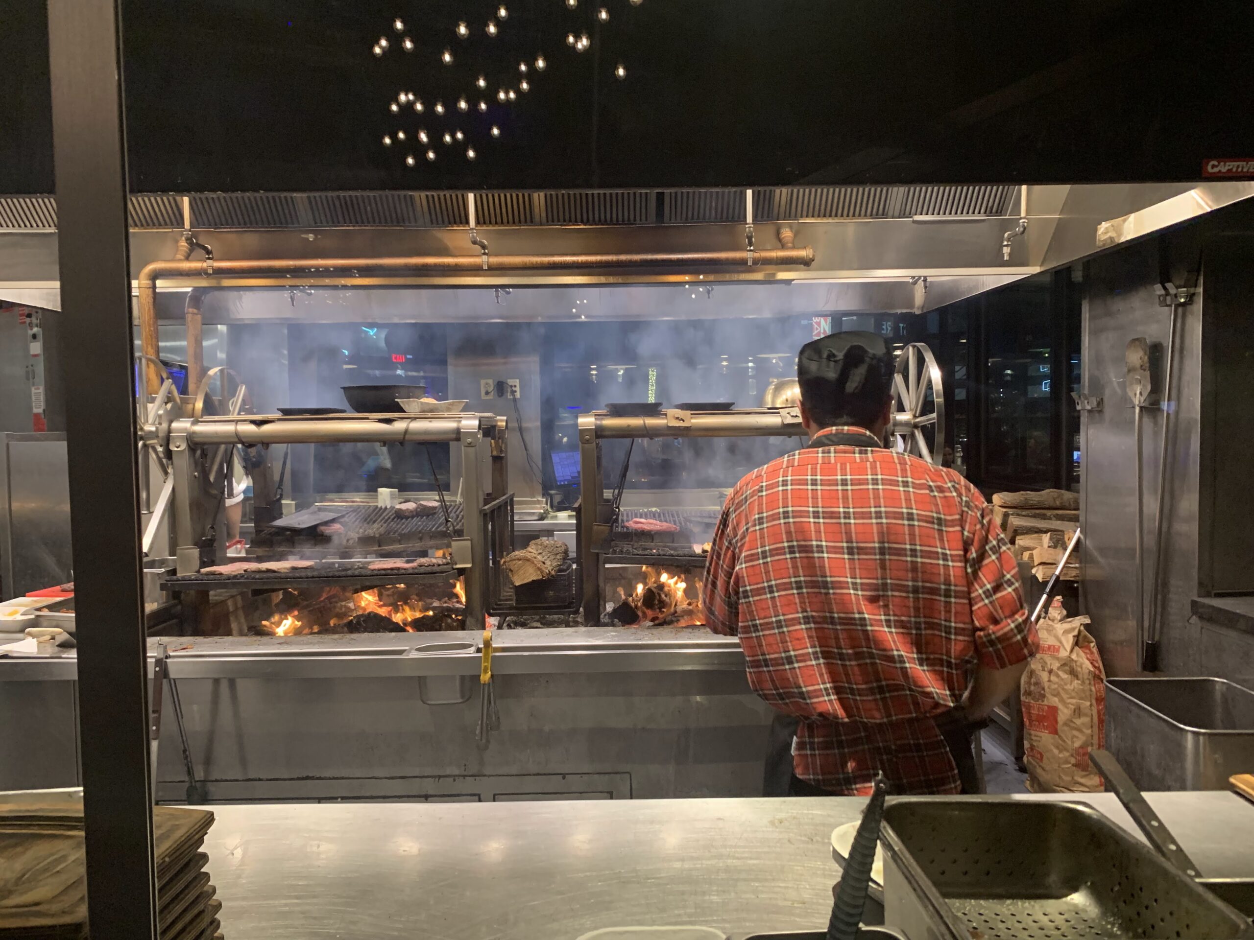 A chef in an orange shirt overlooking rotisserie chicken on the roller in BigFire at Citywalk Orlando Studios Florida