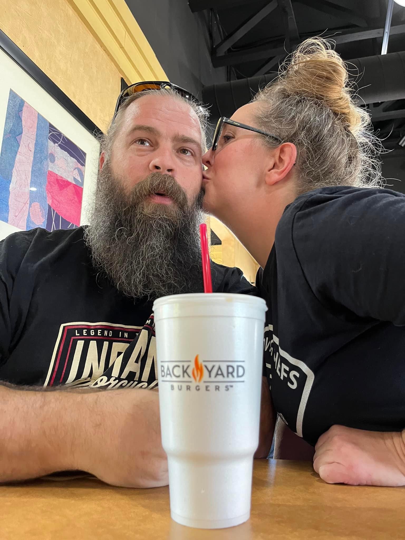 A female kissing a male on the cheek with a backyard burger cup in the foreground.