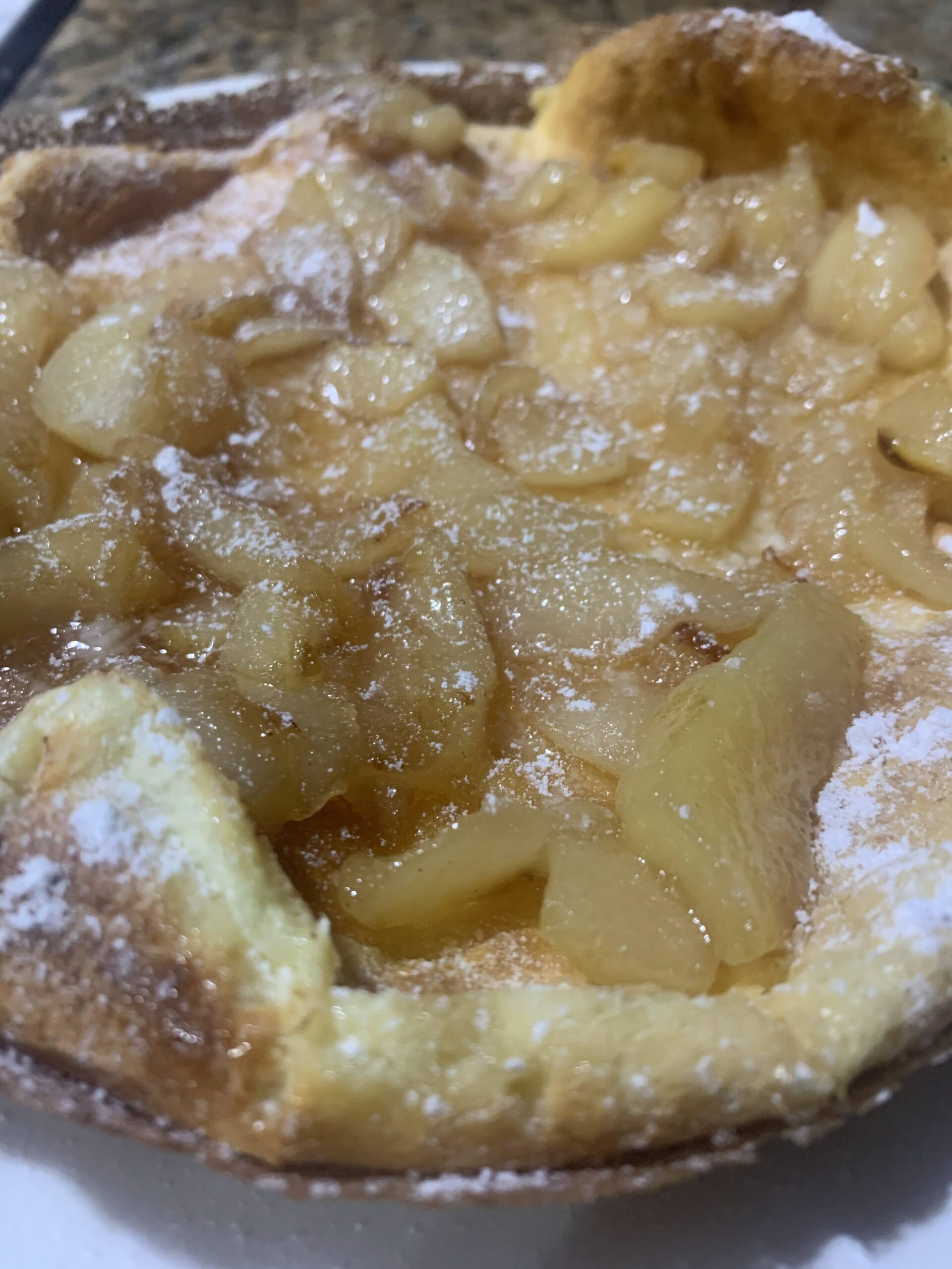 A dutch baby with pears inside topped with powdered sugar.