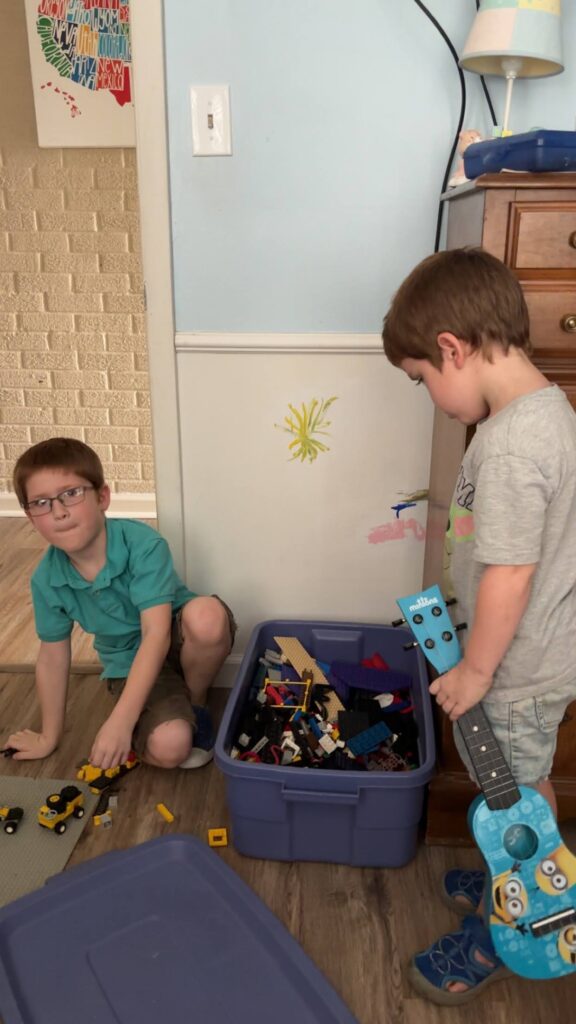 Two boys standing near a toy box filled with legos