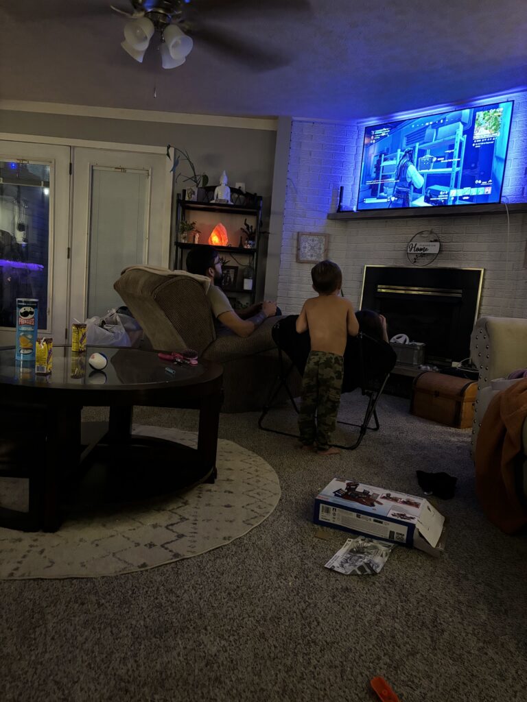 A little boy looking at a tv with his dad sitting in a chair next to him