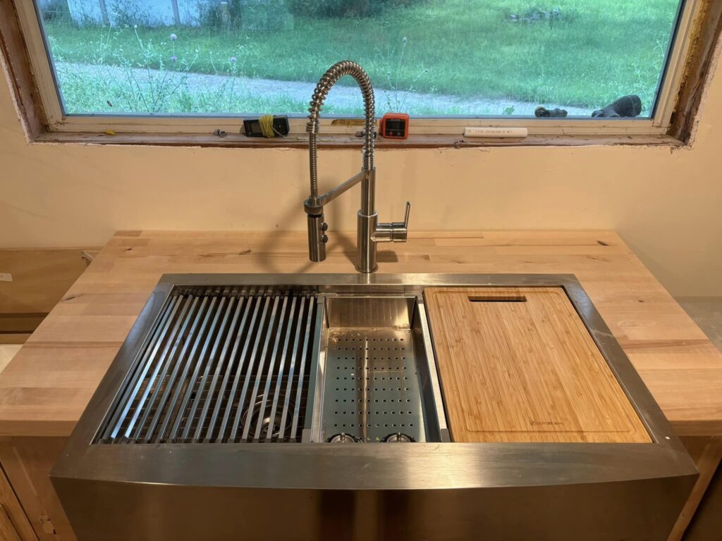 A kitchen sink with a drip strainer, strainer, and cutting board on it.