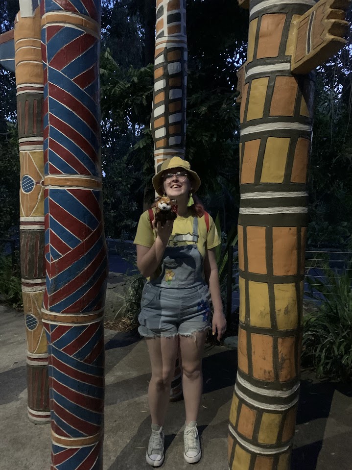 A girl holding a red panda stuffed animal between some tiki poles