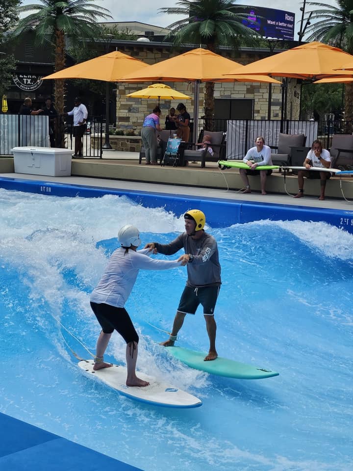 Two people surfing on a wave simulator.