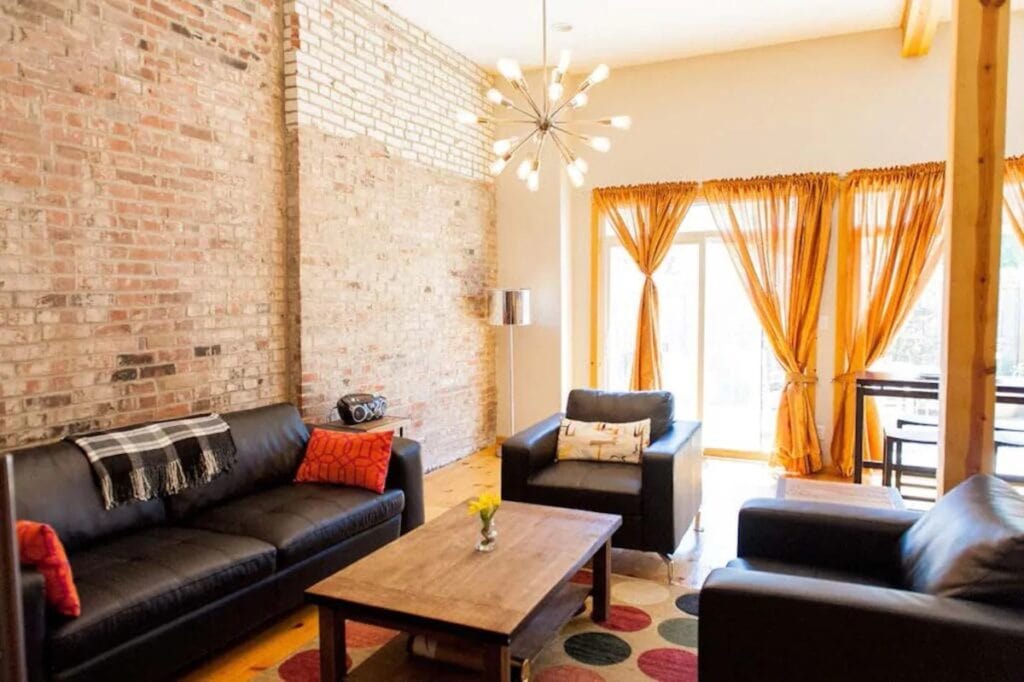 A living room with a brick wall, yellow curtains on the windows, and a black couch