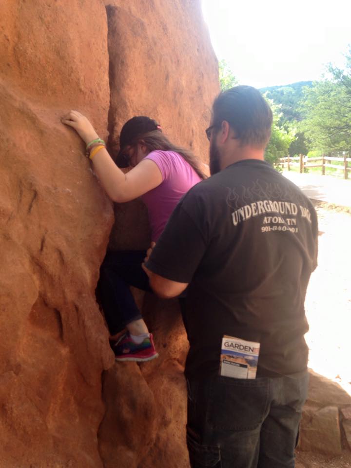 A man helping a girl (his daughter) up a rock