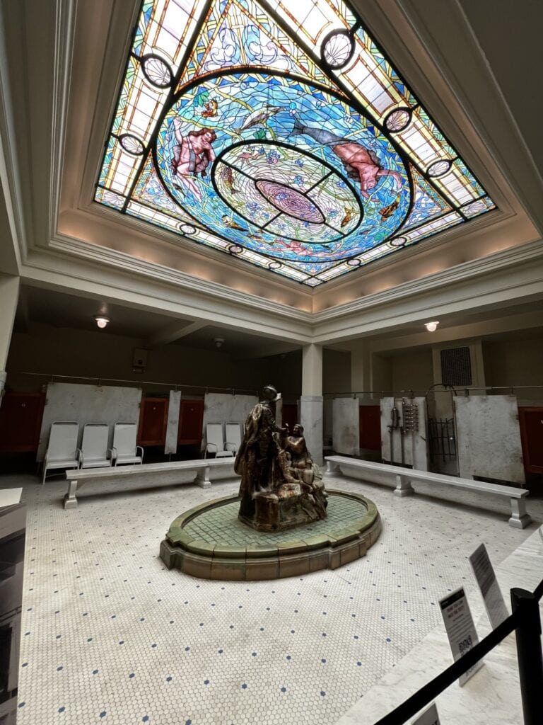 Bath house with a statue in the middle and stained glass ceiling