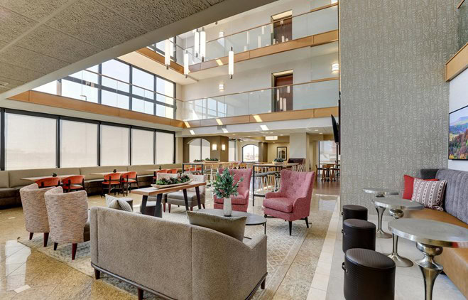 The lobby of a hotel with red chairs sitting in it and two stories of rooms