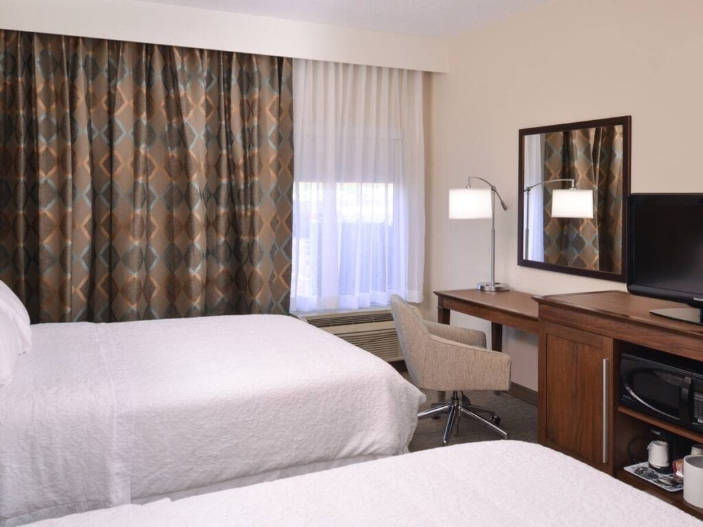 A hotel room with white linens and a curtain