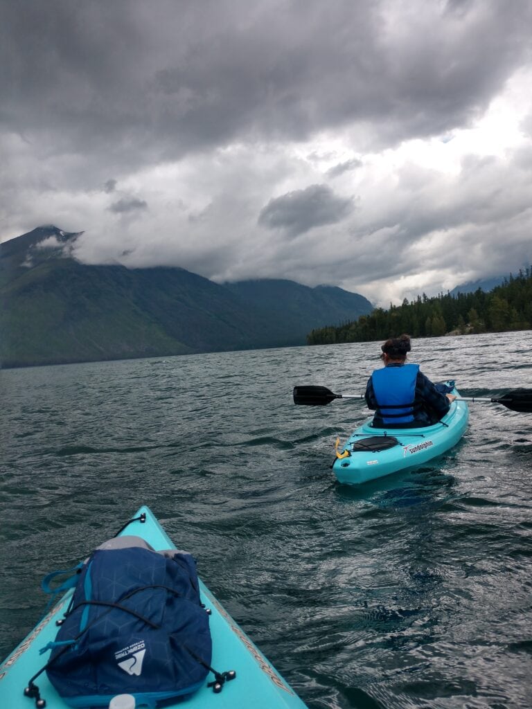 A person kayaking in Glacier National Park with mountains nearby and stormy looking weather