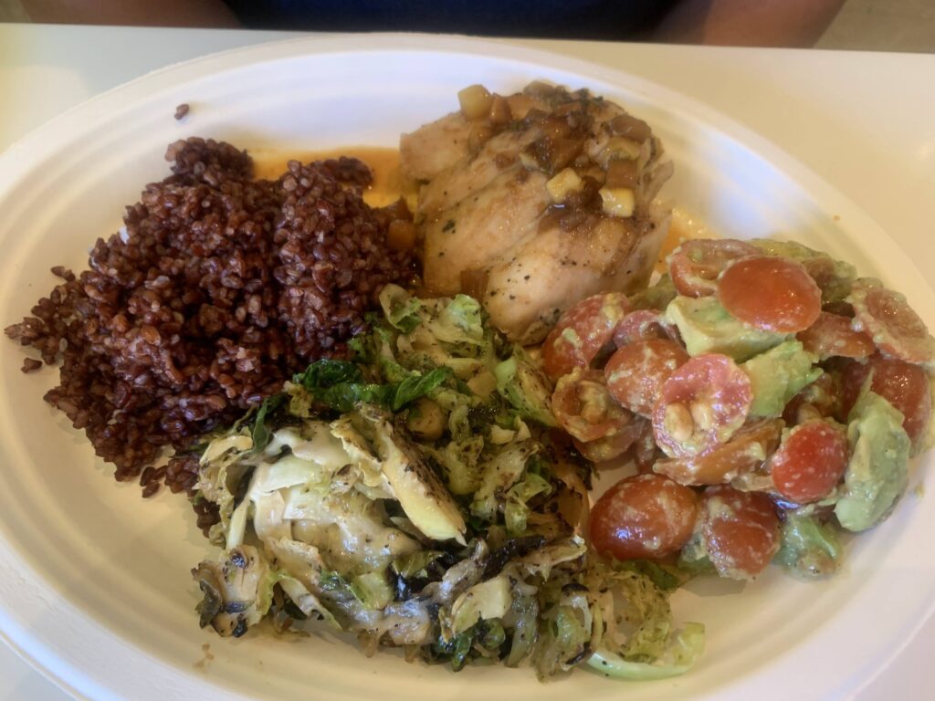 A plate of food with purple rice, Brussels sprouts, and chicken on it