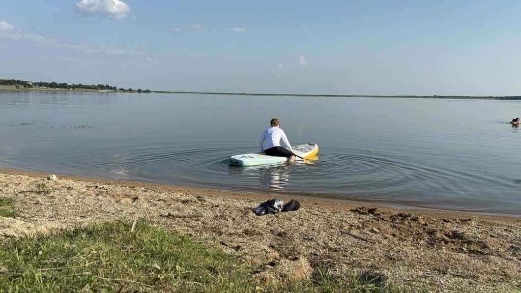 A female getting onto a stand-up paddle board in the water