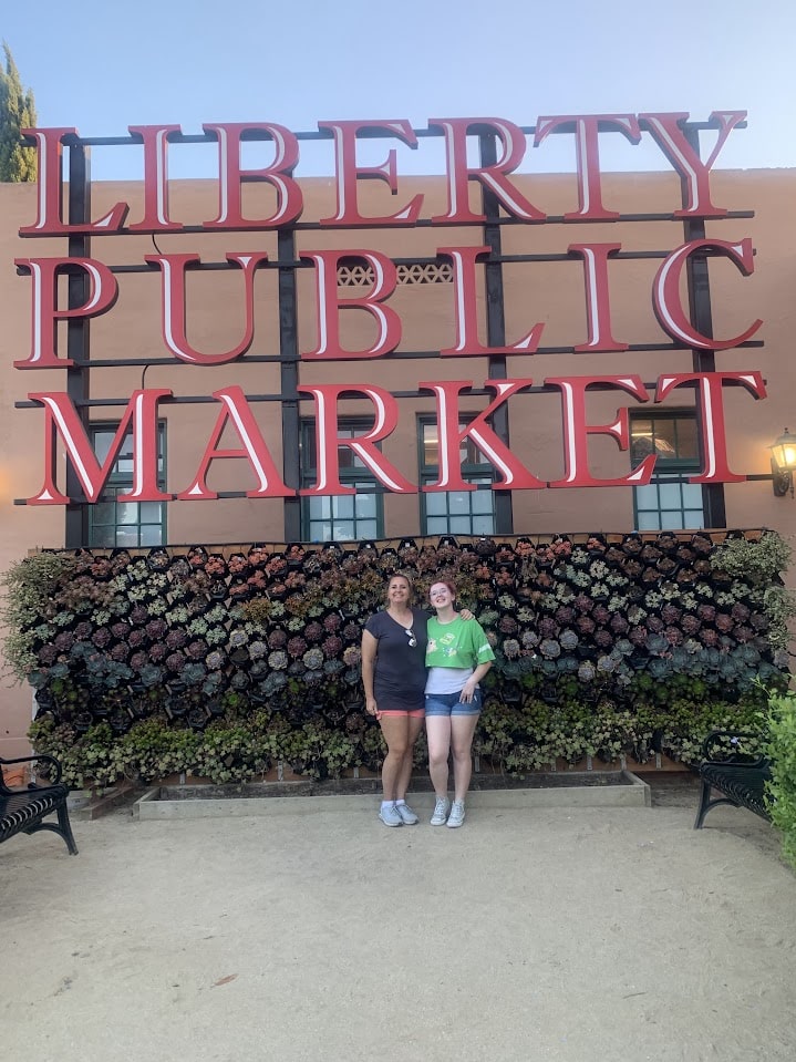 Two females standing in front of a sign that says "Liberty Public Market"