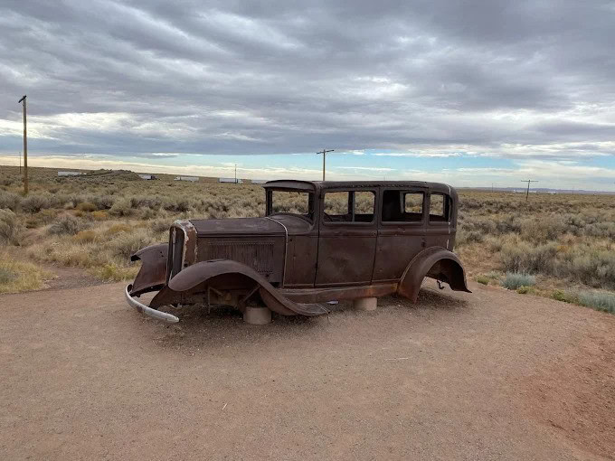 An old rusty car with no wheels left behind to remind people about Route 66's importance.