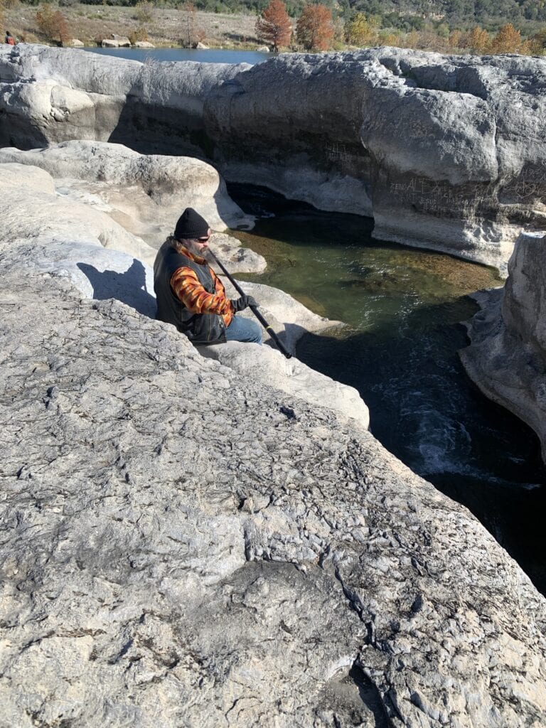 A man sitting on a rock by the water holding his 360