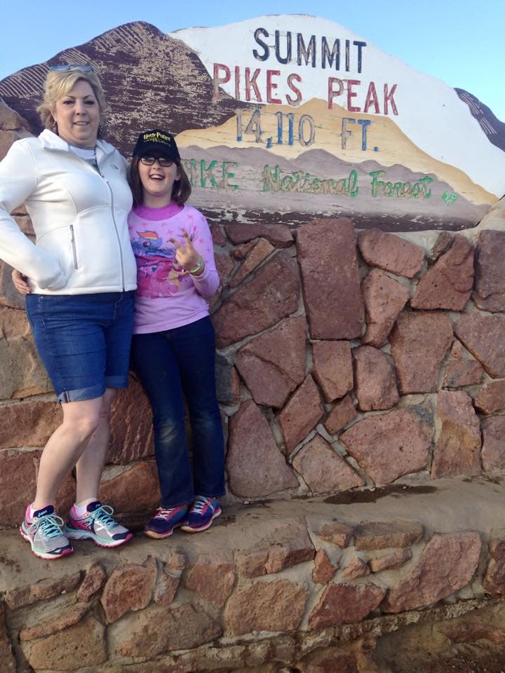 A woman and a girl standing at the Pike's Peek in Colorado Springs Summit sign