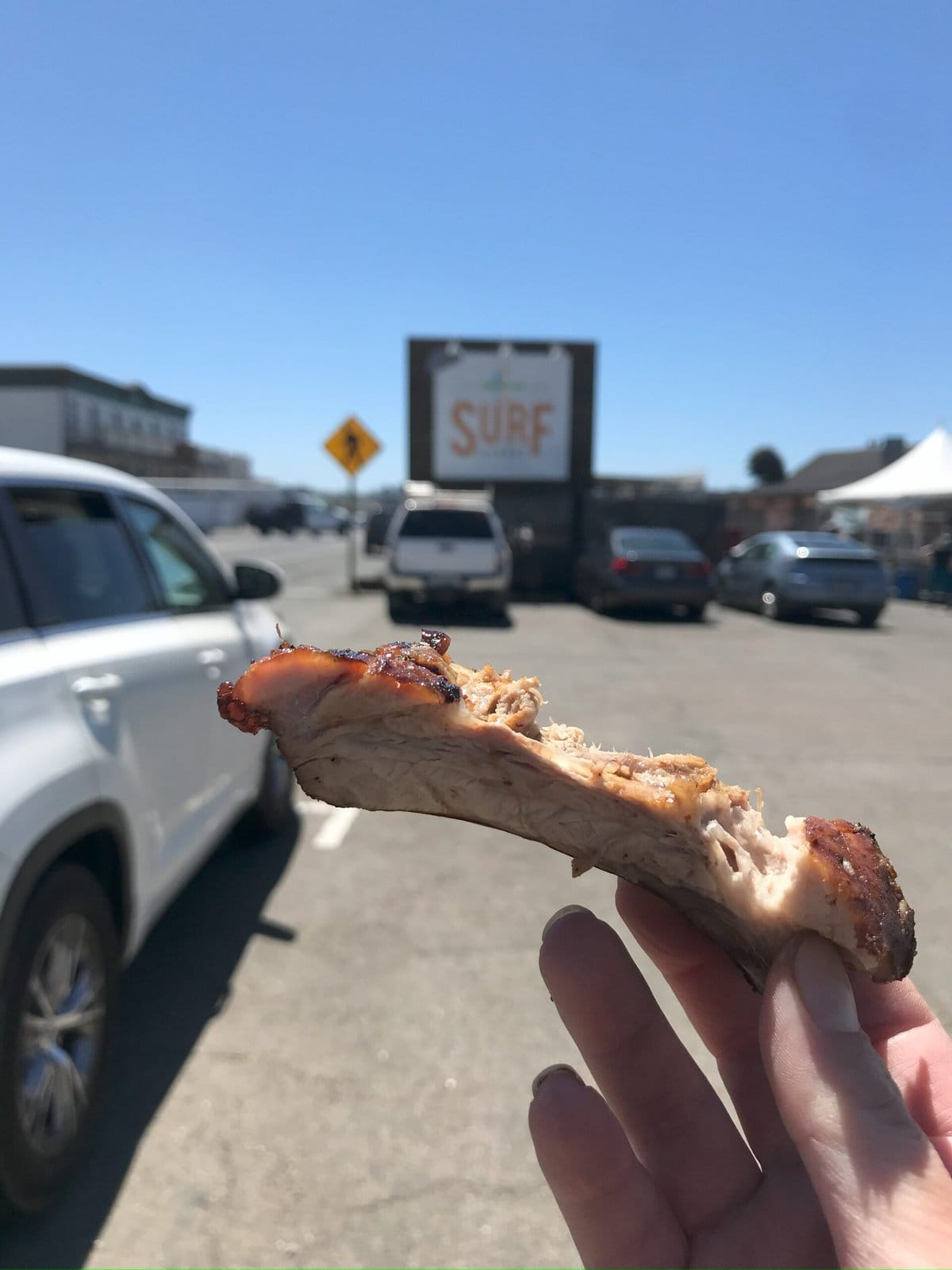 A BBQ rib in the forefront and surf market sign in the back