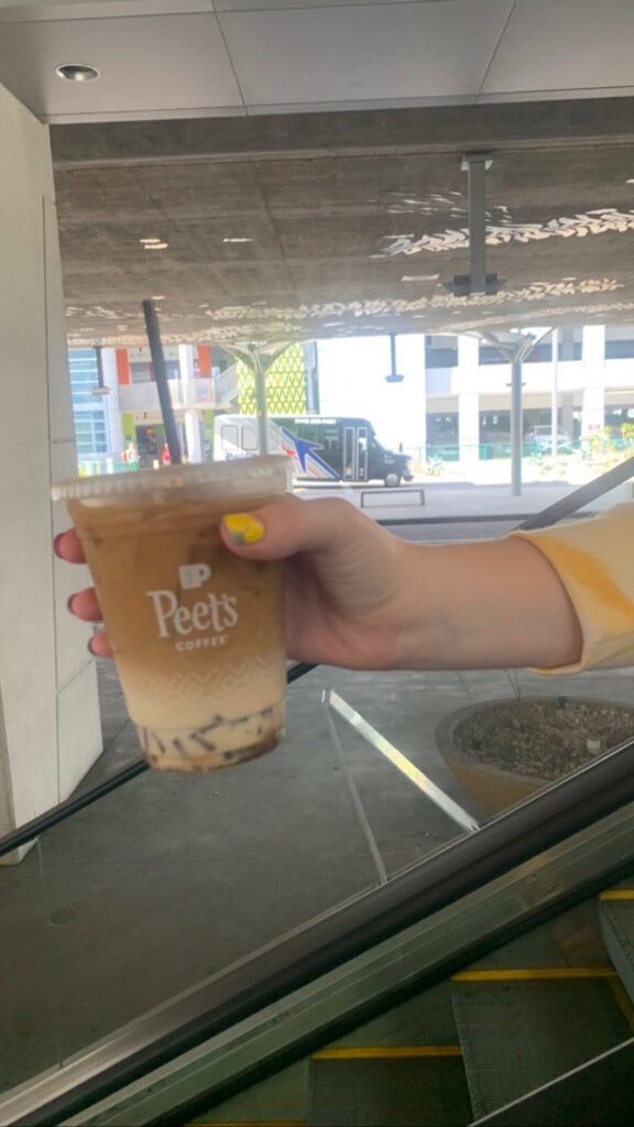 A person holding a Peets coffee going down an escalator