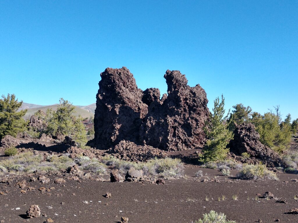 A large rock surrounded by lava and a few trees with a crystal clear blue sky behind it