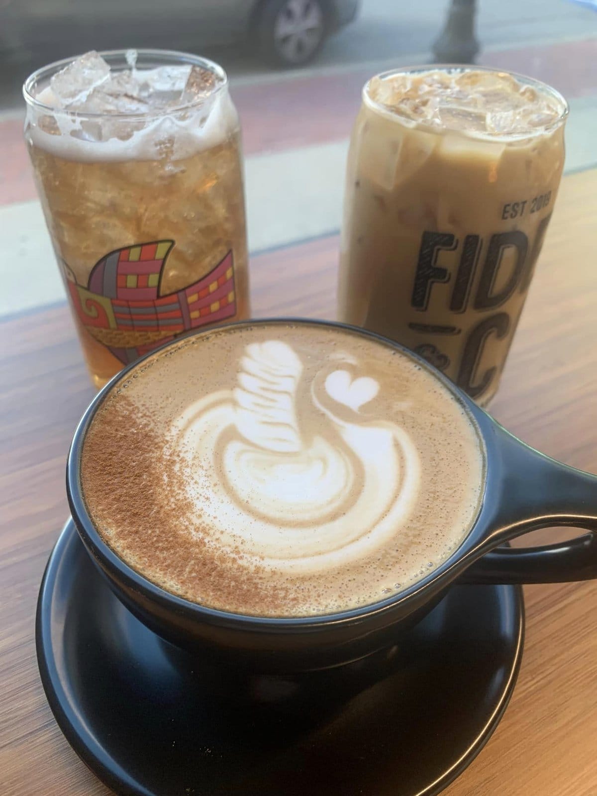 An iced coffee and tea in beer glass cups with a hot coffee in the front that has a swan latte art