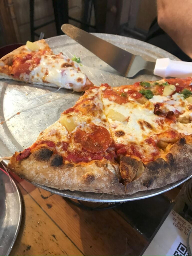 Half ate pizza sitting on top a stand with a wooden table under it