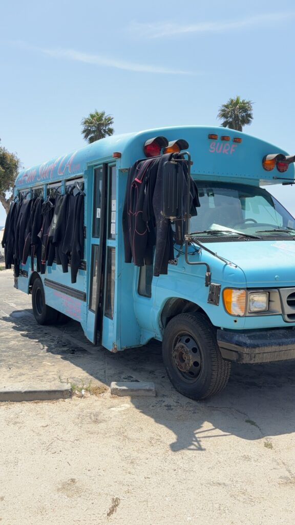 A small blue bus with a bunch of wet suits on it