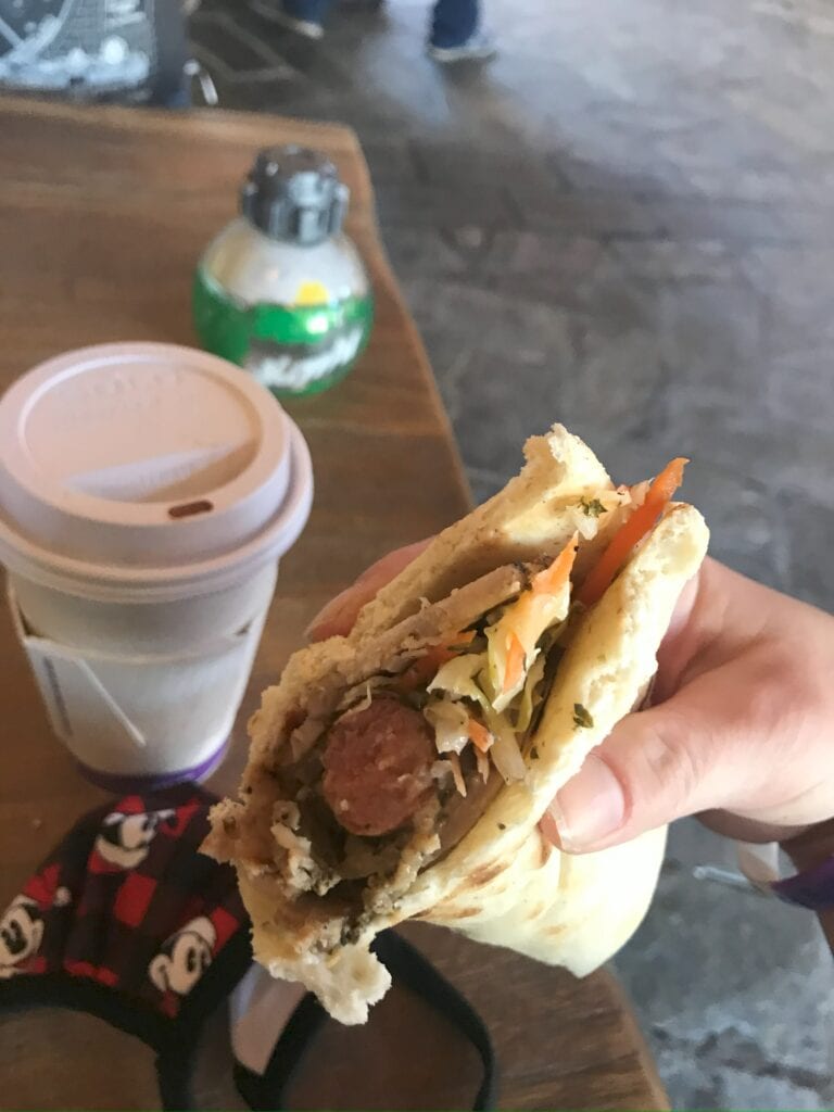 A sausage wrap being held with a coffee and sprite ornament in the background