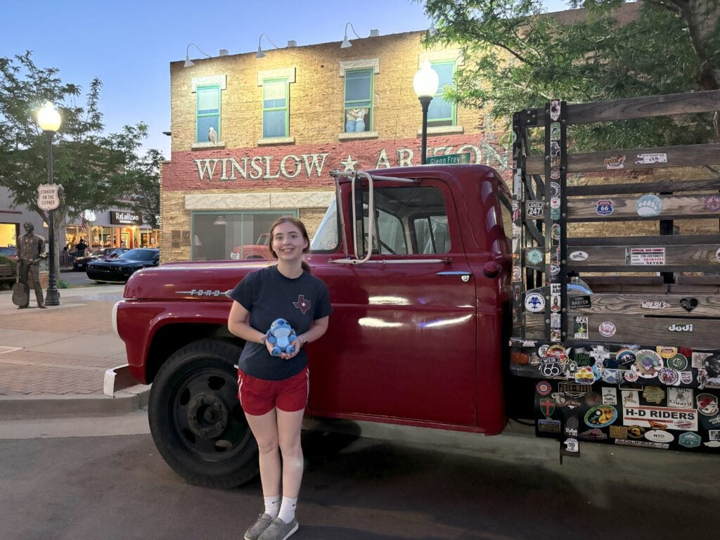 A girl standing on a corner in Winslow, Arizona next to a red flatbed Ford