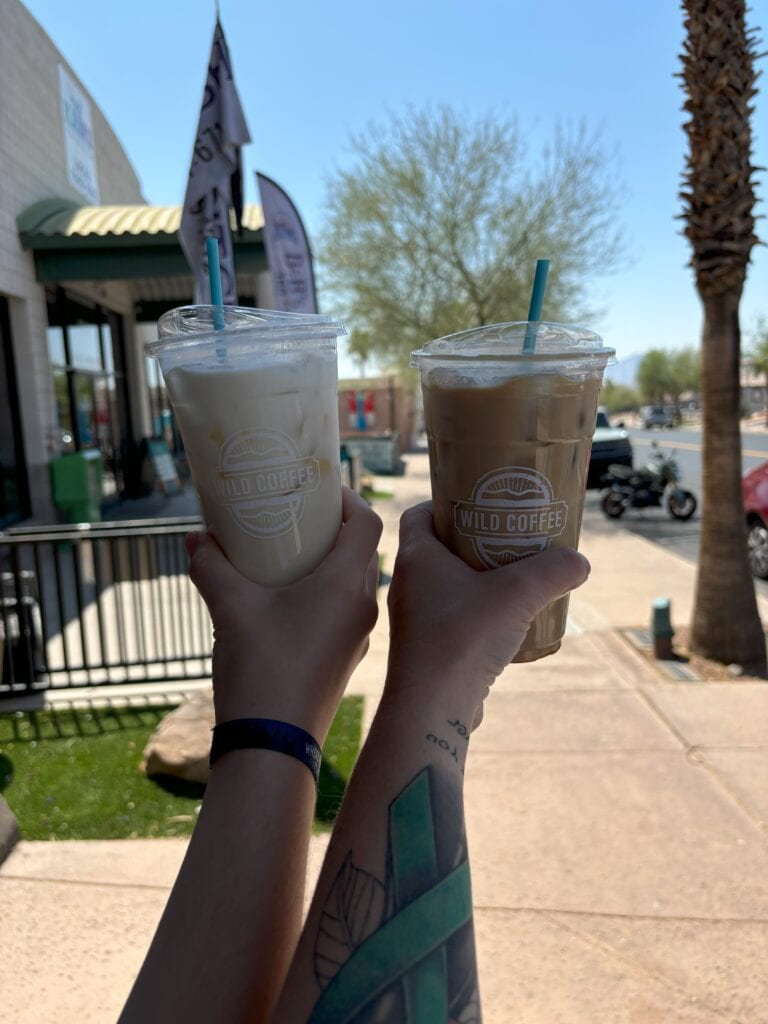 Two arms holding up cold coffees with a town square in the background